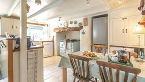 Una cocina con mesa, sillas, cafetera y refrigerador.