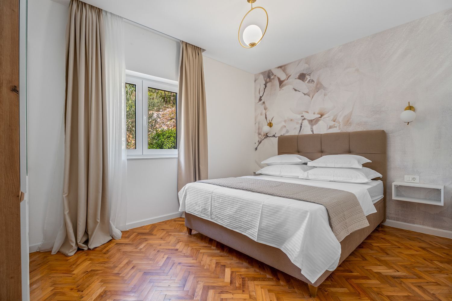 Un dormitorio con cama, cortinas, una ventana, una pared con un mural floral y suelo de madera.