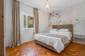 Une chambre à coucher avec un lit, des rideaux, une fenêtre, un mur orné d’une fresque florale et un plancher en bois.