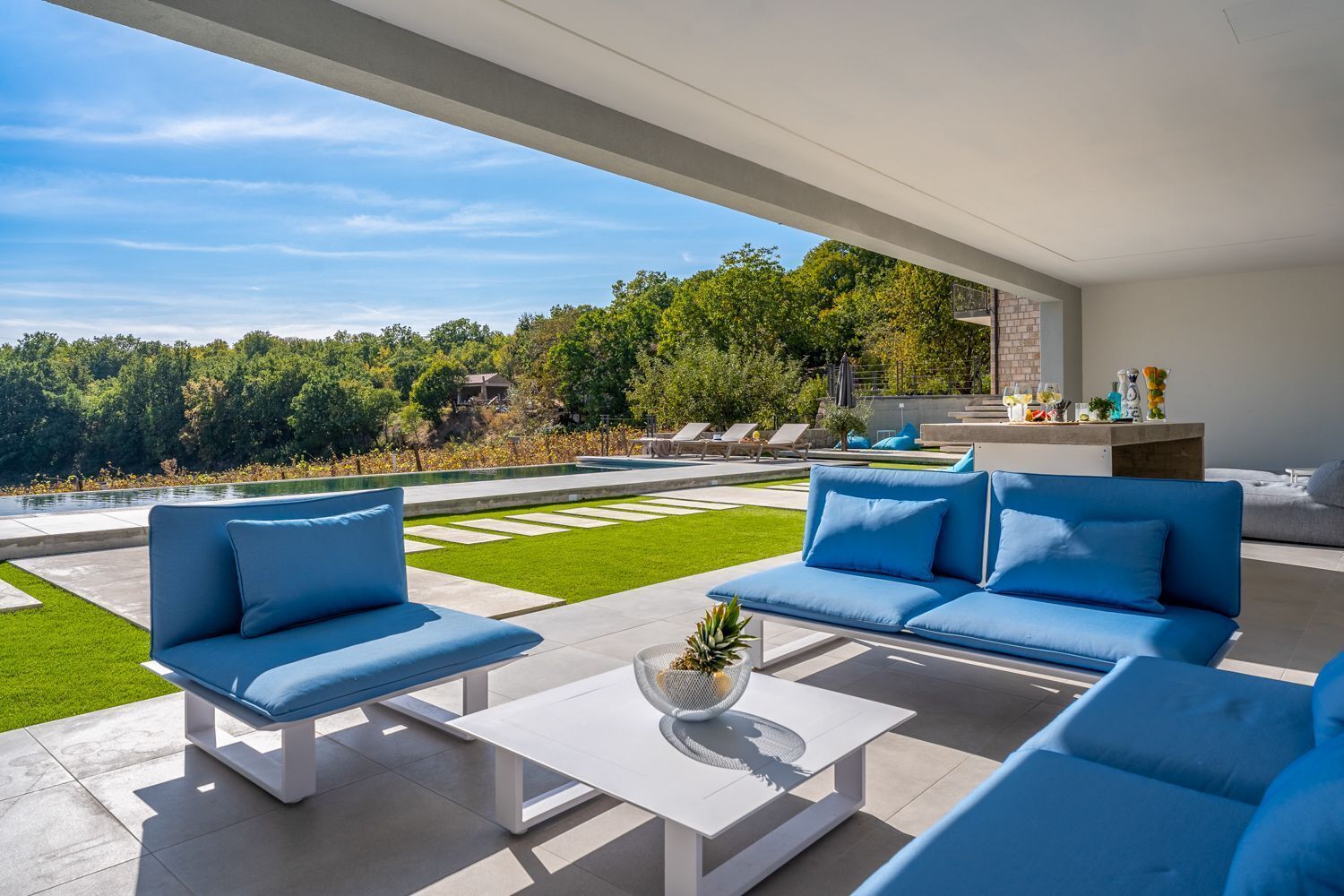 Un espacio al aire libre moderno con piscina, sofás azules y una mesa blanca.