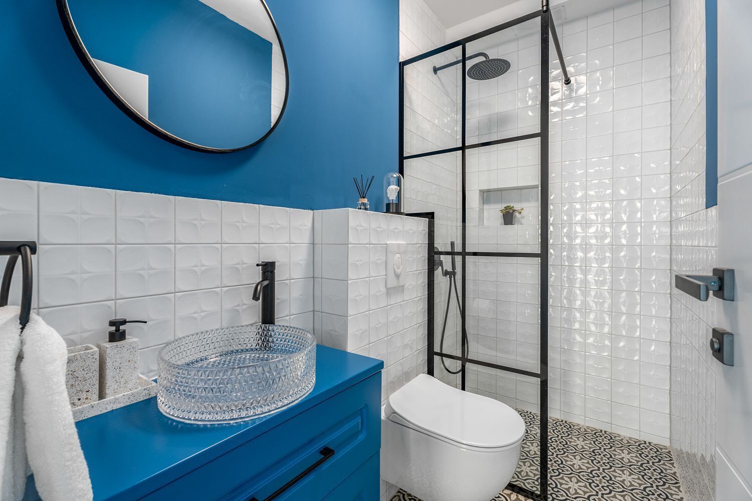 Ein Badezimmer mit blauer Waschtischkommode, einem Glastischwaschbecken, einer weißen Toilette und einer Duschkabine aus Glas.