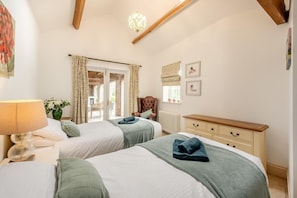 Une chambre avec deux lits, une commode, une chaise et une lampe.