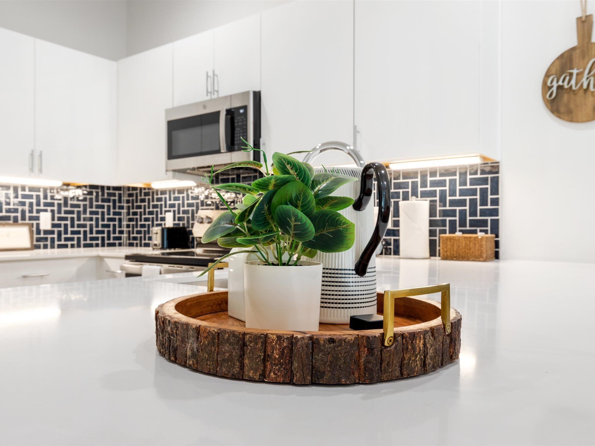 Een moderne keuken met een centraal eiland, een potplant, een waterkoker en een magnetron boven het eiland.