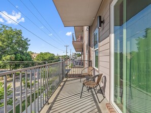 Ein Balkon mit Stuhl, Tisch und Blick auf die Straße sowie umliegende Gebäude.