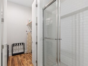 A bathroom with a glass shower enclosure, a wooden floor, and a white tiled wall. - 1BR Getaway at Heart of Oaklawn EV Charger (Dallas)