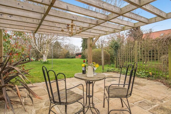 Une terrasse couverte avec une table et des chaises, un lustre et une vue sur le jardin.