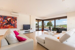 A modern living room with a flat-screen TV, white sofas, a coffee table, and a large window offering a view of the outdoors. - Casa Rogeta - Four Bedroom Villa, Sleeps 8 (Llevant)