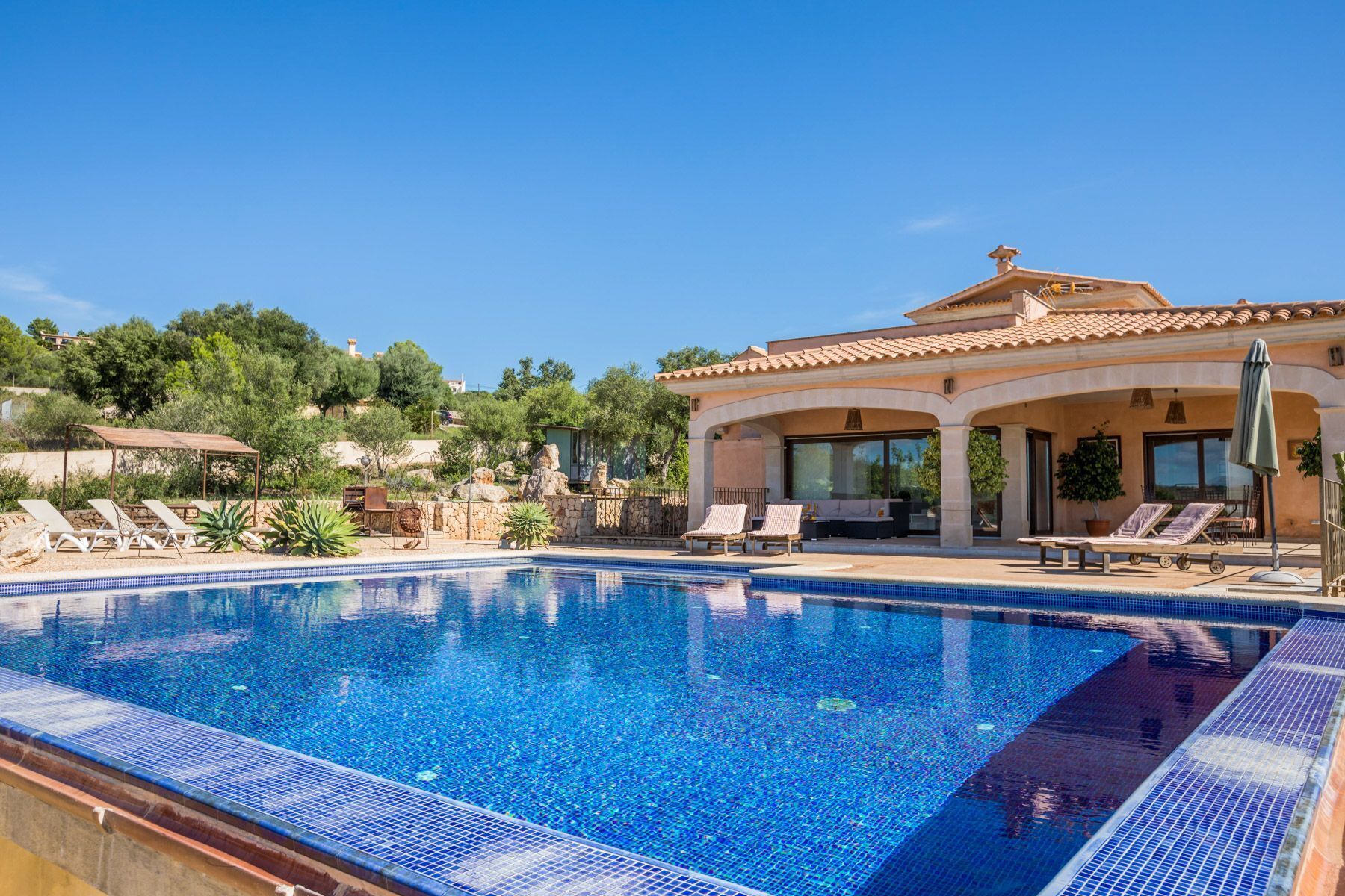 A swimming pool with lounge chairs and a house with a tiled roof.