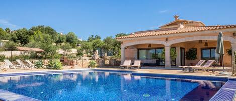 A swimming pool with lounge chairs and a house with a tiled roof.