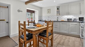 A modern kitchen with white cabinets, a wooden dining table with chairs, and a breakfast setting. - 2 Bed in Hawes (oc-c38234) (Hawes)