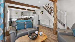 A modern living room with a leather sofa, a coffee table with decorative items, a staircase with wooden accents, and a kitchen in the background. - 2 Bed in Hawes (oc-c38234) (Hawes)