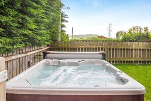 Ein Whirlpool in einem Garten mit Holzzaun und viel Grün.