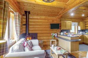 A cozy log cabin interior with a sofa, a fireplace, a kitchen area, and a television mounted on the wall. - 2 Bed in Groesffordd Marli (oc-f39078) (Groesffordd Marli)