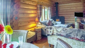 A cozy log cabin interior with a sofa, a table with a vase, a lamp, and a fireplace. - 2 Bed in Groesffordd Marli (oc-g39079) (Groesffordd Marli)