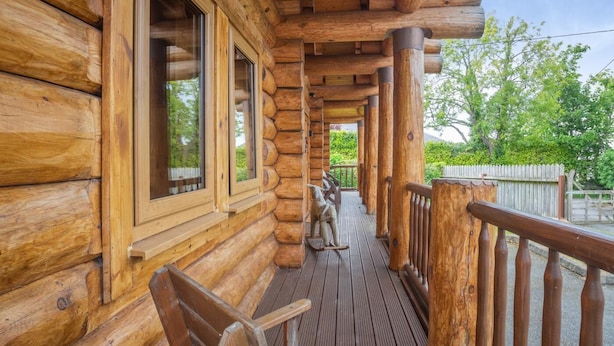 A log cabin with a wooden deck, large windows, and a view of greenery. - 2 Bed in Groesffordd Marli (oc-g39079) (Groesffordd Marli)