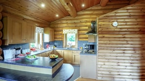 A log cabin interior with a kitchen featuring wooden cabinets, a central island, and a stove. - 2 Bed in Groesffordd Marli (oc-g39079) (Groesffordd Marli)