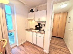 A compact kitchen with a microwave, coffee maker, and utensils, wooden flooring, and a view through a window. - Gemutliches Studio im 2.og in Sellin mit Balkon (Sellin)