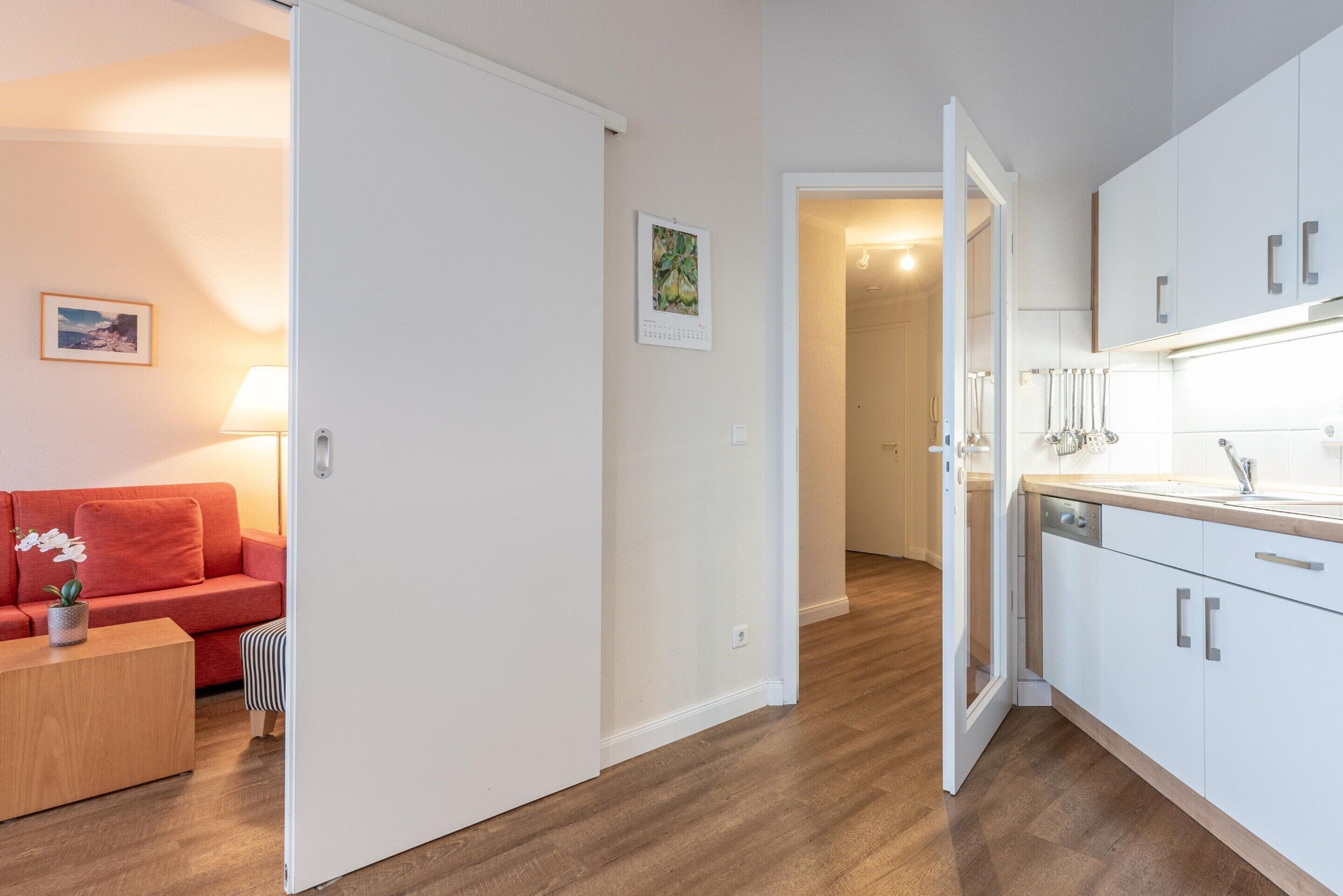 A modern apartment with a kitchen, a living area with a sofa and a small table, and a hallway leading to another room.