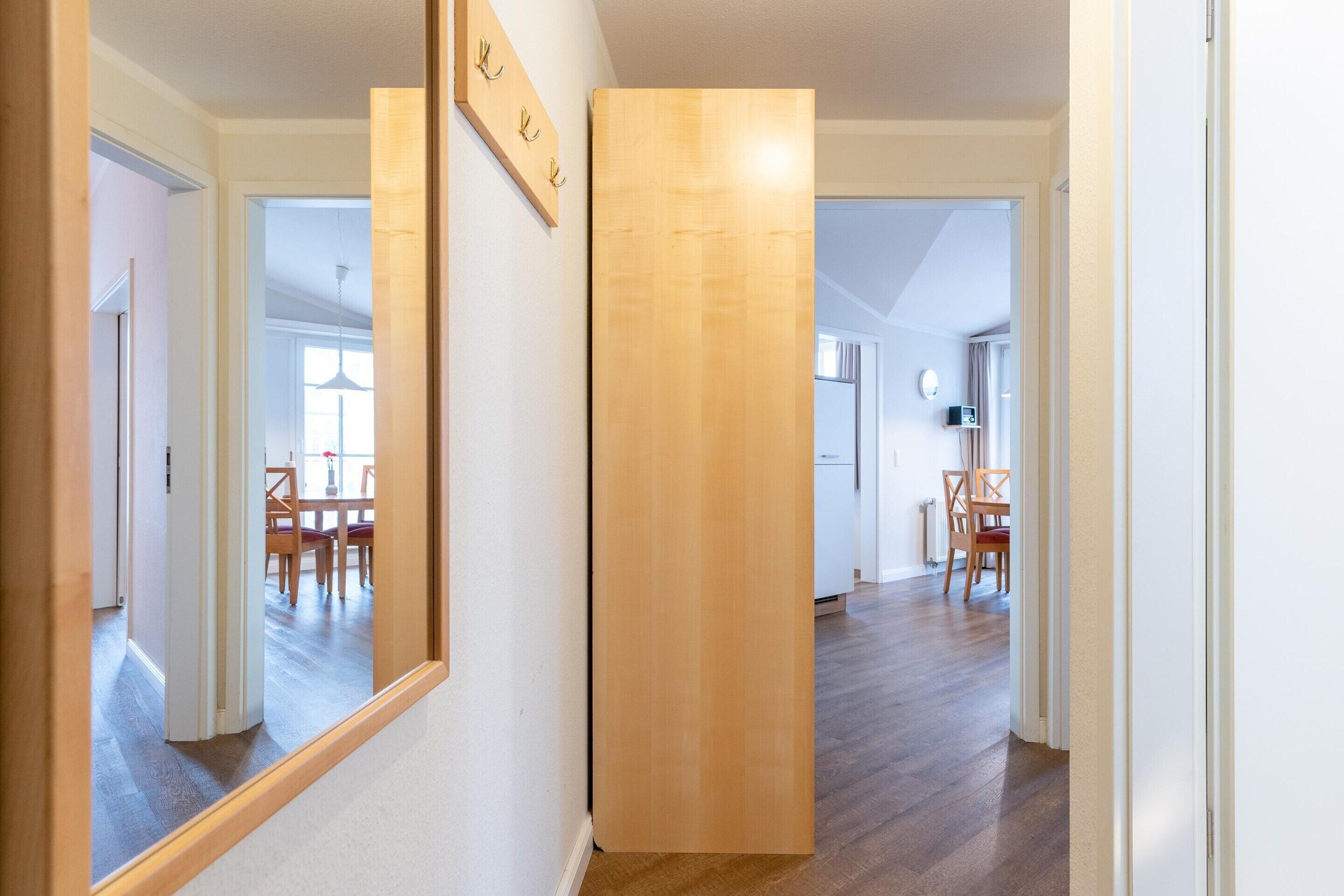 A hallway with wooden flooring, a mirror, and a wooden column. There are doors leading to other rooms.