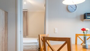 A room with a bed, a wooden chair, a table with a vase, and a clock on the wall. - Geschmackvoll Eingerichtete Ferienwohnung mit Grossem Balkon in Sellin (Sellin)