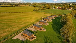 A row of wooden cabins with a grassy field in the foreground and a rural landscape in the background. - 2 Bed in Athelington (oc-d35071) (Athelington)