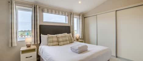 A bedroom with a bed, bedside tables, a nightstand, a window with curtains, and a view of the outside.