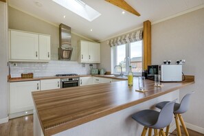 A modern kitchen with white cabinets, a wooden countertop, a gas stove, and a built-in oven. There are two bar stools and a window with a view. - 2 Bed in Athelington (oc-d35071) (Athelington)