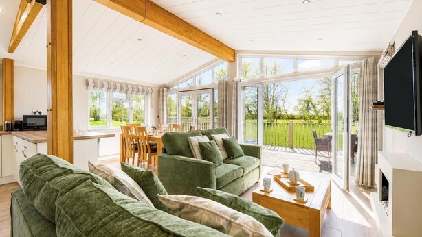 A spacious living area with a large green sofa set, a wooden dining table, and a television mounted on the wall. - 2 Bed in Athelington (oc-d35071) (Athelington)