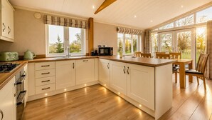 A modern kitchen with white cabinets, a wooden countertop, and a dining area with a table and chairs. - 2 Bed in Athelington (oc-d35071) (Athelington)