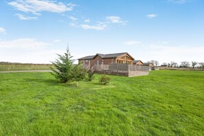 Ein eingeschossiges Holzhaus mit einem eingezäunten Garten, umgeben von einer grünen Wiese.