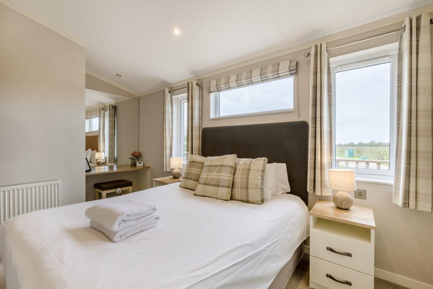 A hotel room with a large bed, bedside tables, a mirror, and a window with curtains.