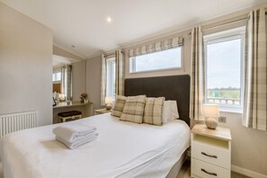 Ein Hotelzimmer mit einem großen Bett, Nachttischen, einem Spiegel und einem Fenster mit Vorhängen.