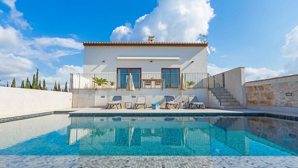 Una casa moderna de dos pisos con piscina, asientos exteriores y un cielo azul despejado.