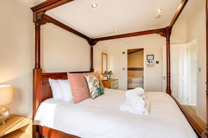 A four-poster bed with white linens and a pink pillow, a wooden nightstand with a lamp, and a mirror on the wall. - 1 Bed in Athelington (oc-c35073) (Athelington)