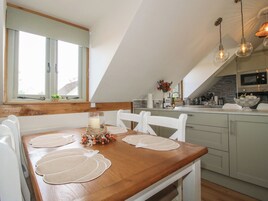 Un comedor con una mesa de madera, sillas blancas y una ventana con persianas.