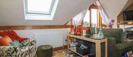 Un dormitorio estilo loft acogedor con tragaluz, un sofá verde, una mesa de madera con libros y un televisor.