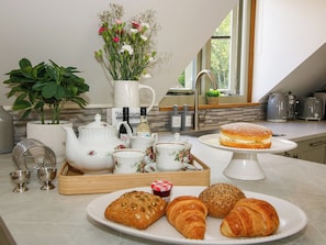 Una encimera de cocina con un juego de té, un pastel, bollería y una planta en maceta.