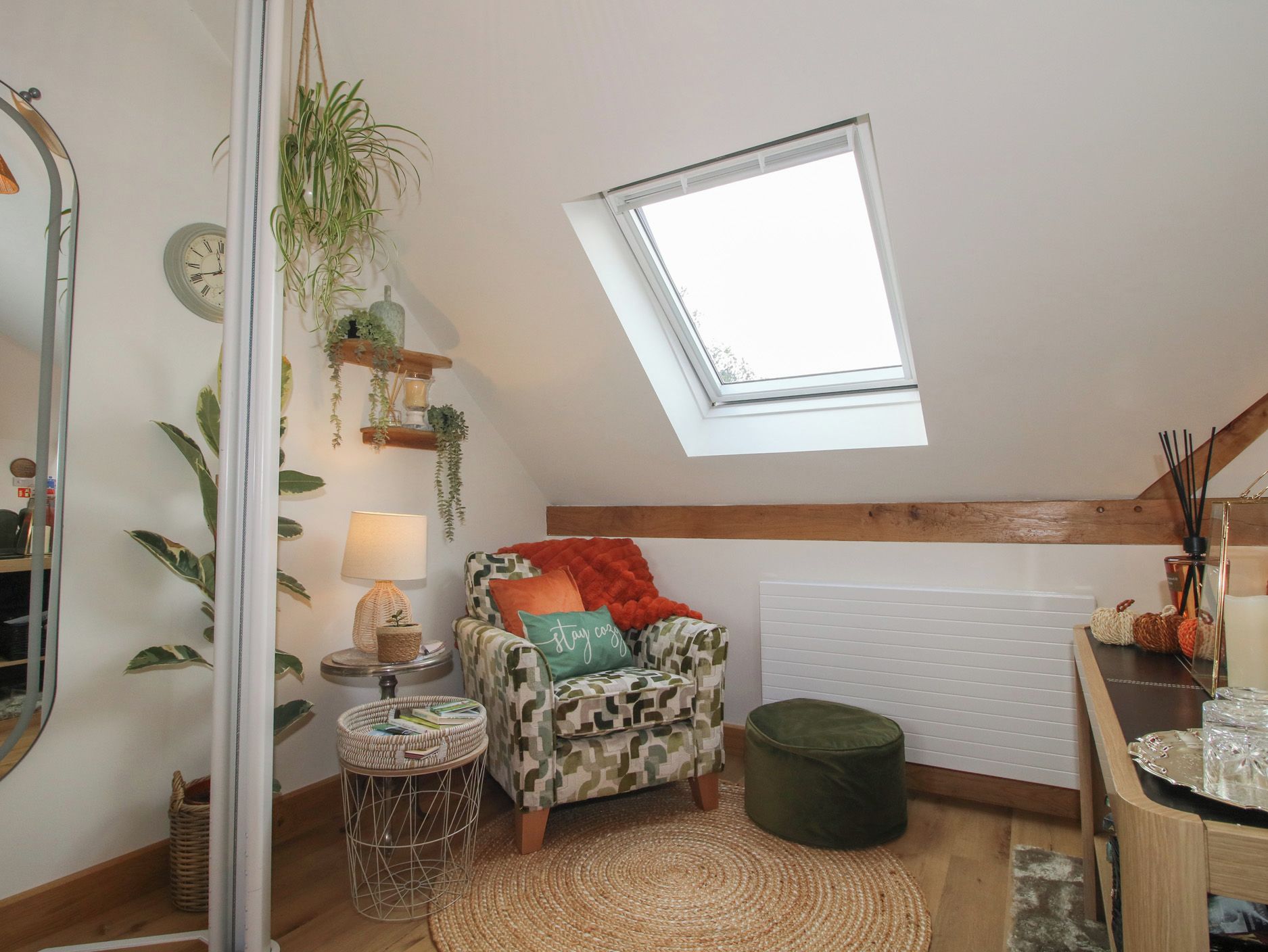 A cozy loft bedroom with a skylight, a patterned armchair, a small round table, and a green ottoman.