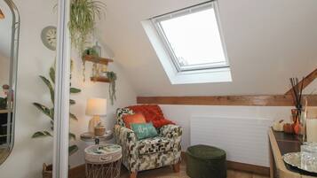 A cozy loft bedroom with a skylight, a patterned armchair, a small round table, and a green ottoman.