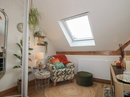 Un dormitorio tipo loft acogedor con tragaluces, un sillón estampado, una mesita redonda pequeña y un reposapiés verde.