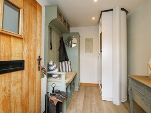 Un pasillo con una puerta de madera, un banco con un cojín a rayas, un espejo y un armario blanco.