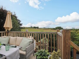 A wooden deck with a wicker sofa, a table with green glassware, and a view of a green field.