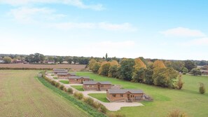 A row of single-story cabins with a grassy field and trees in the background. - 1 Bed in Athelington (oc-l35074) (Athelington)