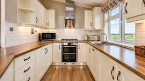 A modern kitchen with white cabinets, a wooden countertop, a built-in oven, a microwave, and a window with a view of the outdoors. - 3 Bed in Athelington (oc-p35076) (Athelington)