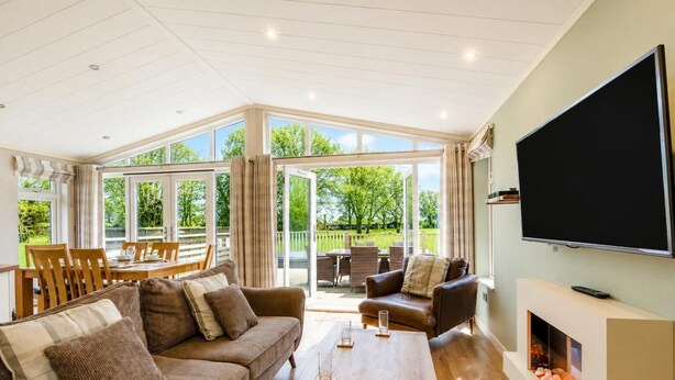 A spacious living room with a large TV, a fireplace, and a dining area with outdoor views. - 3 Bed in Athelington (oc-p35076) (Athelington)