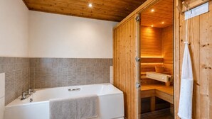 Un bany modern amb sostre de fusta, una banyera gran i una sauna visible a través d'una porta oberta.