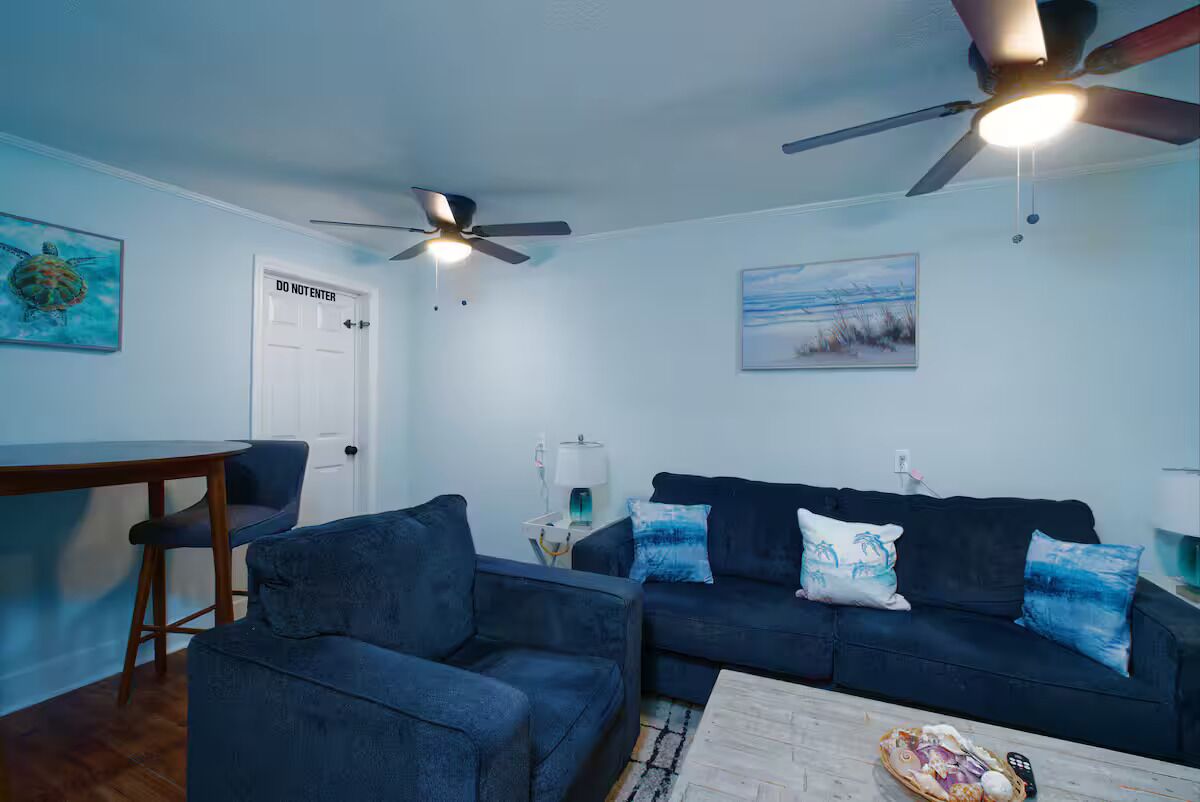 A living room with a dark blue sofa, a coffee table, a ceiling fan, and a painting on the wall.