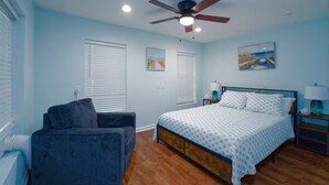 A bedroom with a bed, a ceiling fan, a nightstand, a lamp, and a window with blinds.