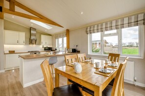 A modern kitchen with a central island, wooden chairs, and a dining table set for breakfast. - 2 Bed in Athelington (oc-v35079) (Athelington)
