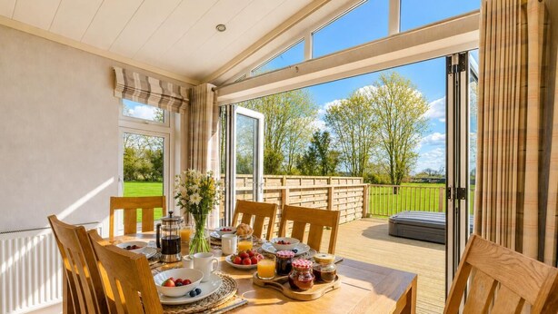 Un coin repas avec une table mise pour le petit-déjeuner, une vue sur l’extérieur et une terrasse en bois.